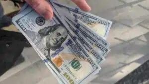 A musician holding a stack of dollar bills in front of a staircase, showcasing their success in money management.