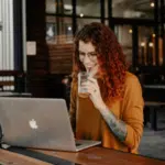 A woman sitting at a table with a laptop working on email marketing.