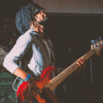 A man with dreadlocks playing a bass at a concert by black owned labels.