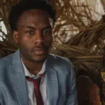 A man in a suit sitting in front of a strategically placed pile of straw.