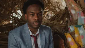 A man in a suit sitting in front of a strategically placed pile of straw.