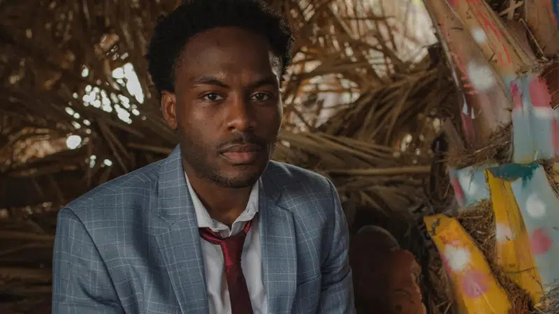 A man in a suit sitting in front of a strategically placed pile of straw.