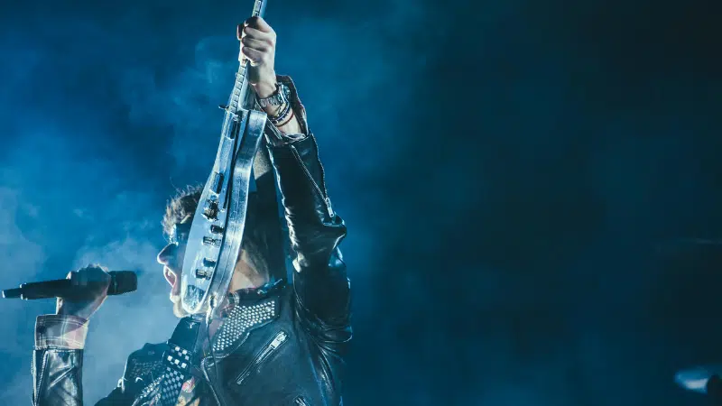 A man in a leather jacket is holding up a guitar for a record label.