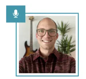 A man with glasses and a microphone conducting a Q&A session in front of a plant.