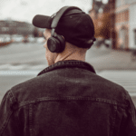 A man wearing headphones is crossing the street while listening to a third party playlist.