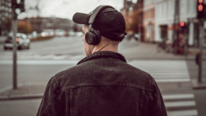 A man wearing headphones is crossing the street while listening to a third party playlist.