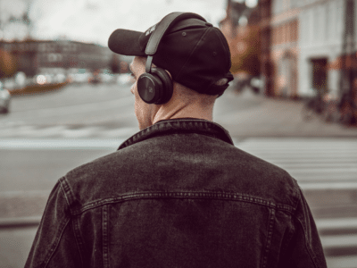 A man wearing headphones is crossing the street while listening to a third party playlist.