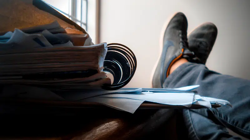 A person's feet resting on a pile of papers.