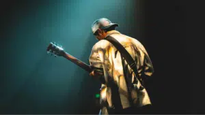 A man strumming a guitar in a dimly lit room, lost in the pursuit of his musical goals.