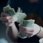 A person in a blue shirt counting a stack of US dollar bills from mechanical royalties.