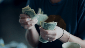A person in a blue shirt counting a stack of US dollar bills from mechanical royalties.
