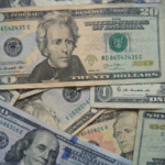 Assorted U.S. dollar bills including SplitShare twenties, hundreds, and ones, haphazardly arranged and overlapping.
