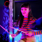 A woman playing drums in a dark room for fans.