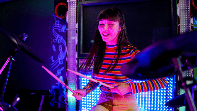 A woman playing drums in a dark room for fans.