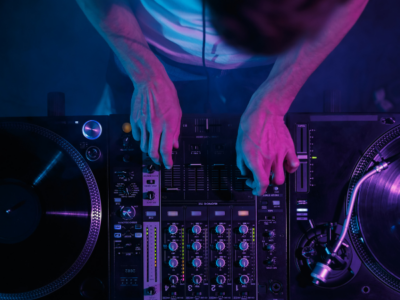 A person operates a DJ mixer and two turntables under purple and blue lighting, adjusting controls and playing vinyl records—showcasing essential music promotion tips in action.