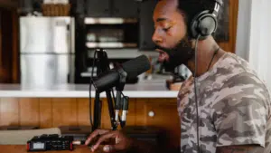 A man in headphones is sitting in front of a microphone, surrounded by his back catalog.