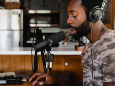 A man in headphones is sitting in front of a microphone, surrounded by his back catalog.