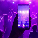 A person holding a phone up to a crowd at a concert.