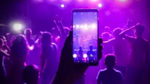 A person holding a phone up to a crowd at a concert.