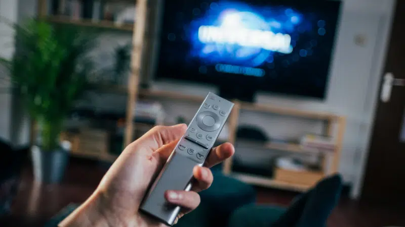 A person with a remote control in front of a TV, using sync licensing.