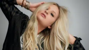 A young woman with long blonde hair featured in a pose on a gray background.