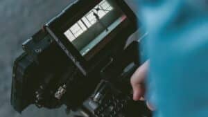 A person holding a video camera and distributing content via tablet.