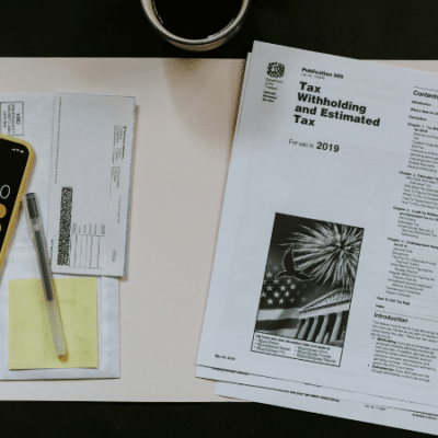 Amidst tax documents and forms for 2019, a smartphone with a calculator app open sits on the desk beside a pen, an envelope, and a cup of coffee. As an independent musician juggling royalties and expenses, preparing taxes requires focused attention.