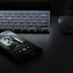 A cell phone sitting on a desk next to a keyboard, showcasing Spotify.