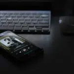 A cell phone sitting on a desk next to a keyboard, showcasing Spotify.