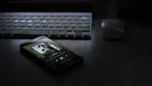 A cell phone sitting on a desk next to a keyboard, showcasing Spotify.