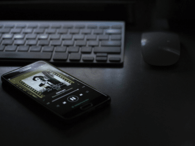 A cell phone sitting on a desk next to a keyboard, showcasing Spotify.