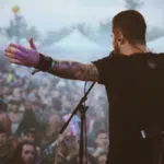 A man touring at a music festival with his arms out in front of a crowd.