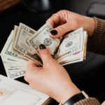A symphonic woman's hand holding a stack of money on a desk.