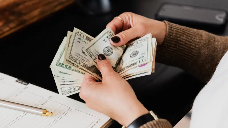 A symphonic woman's hand holding a stack of money on a desk.