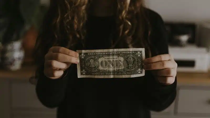 A woman showcasing advances in her kitchen with a one dollar bill.