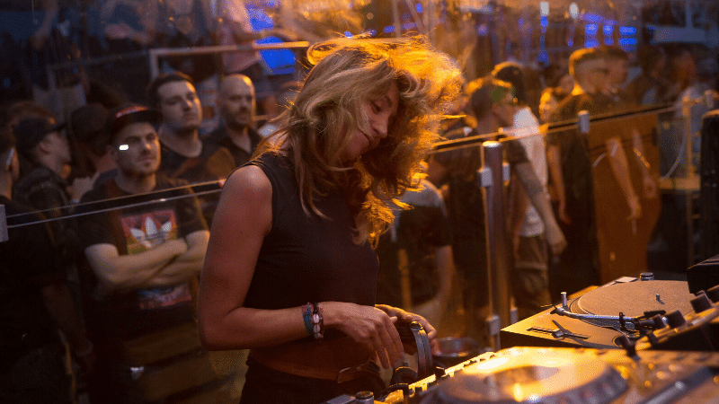 A women-led DJ playing music for a crowd.