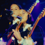 Two women-owned labels playing guitars in front of a microphone.