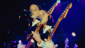 Two women-owned labels playing guitars in front of a microphone.