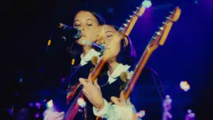 Two women-owned labels playing guitars in front of a microphone.