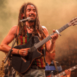 A man playing an acoustic guitar with dreadlocks, evoking reggae vibes.