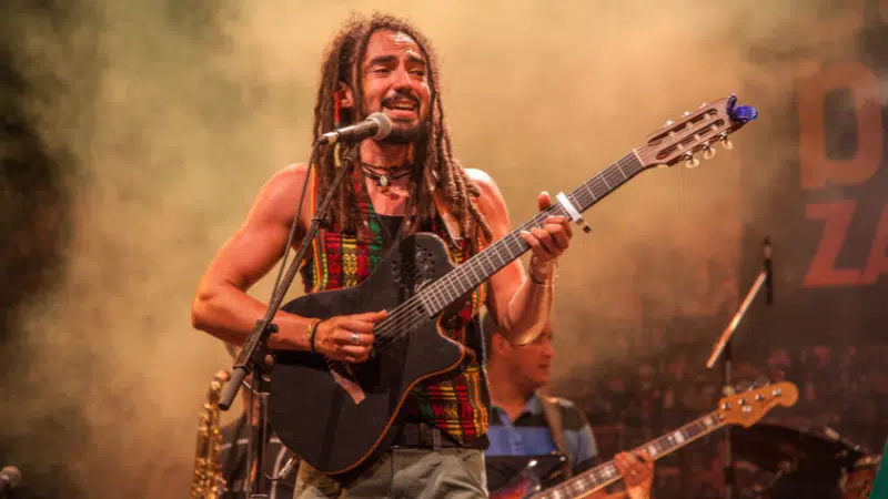 A man playing an acoustic guitar with dreadlocks, evoking reggae vibes.