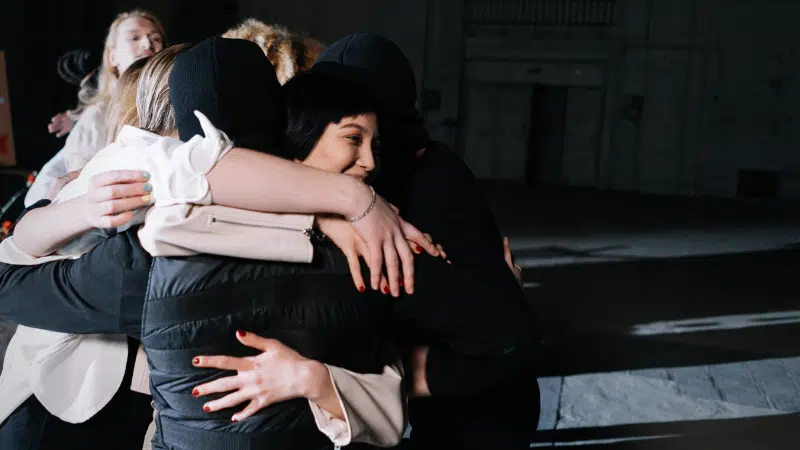 A group of people embracing in a dark room to promote mental health.