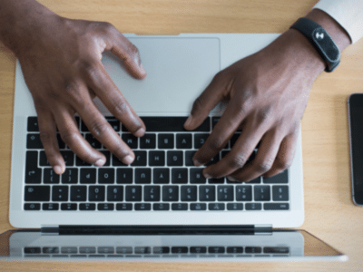 Hands typing on a laptop with a cell phone, Instagram.