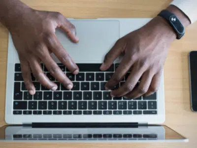 Hands typing on a laptop with a cell phone, Instagram.