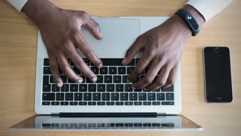 Hands typing on a laptop with a cell phone, Instagram.