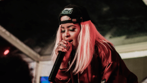 A woman with pink hair singing into a microphone during a music distribution event.