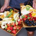 A man holding two trays of healthy fruit.