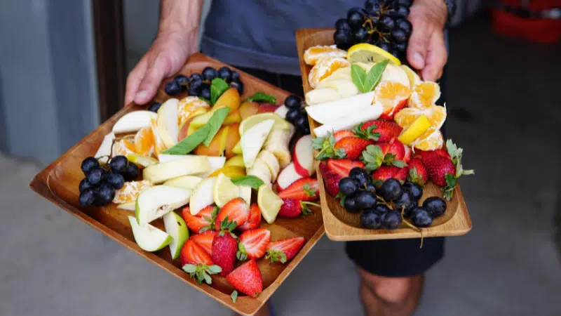 A man holding two trays of healthy fruit.