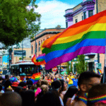 A crowd of prideful people walking down a street with a rainbow flag.