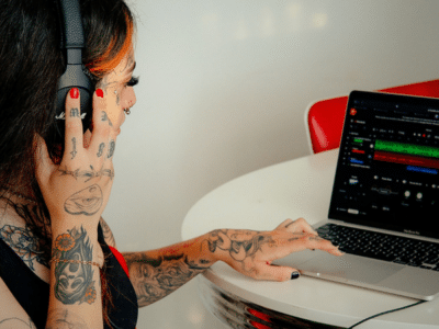 A person with tattoos, deeply engrossed in their work, wears headphones and uses a laptop at a table, mastering the art of social media marketing.